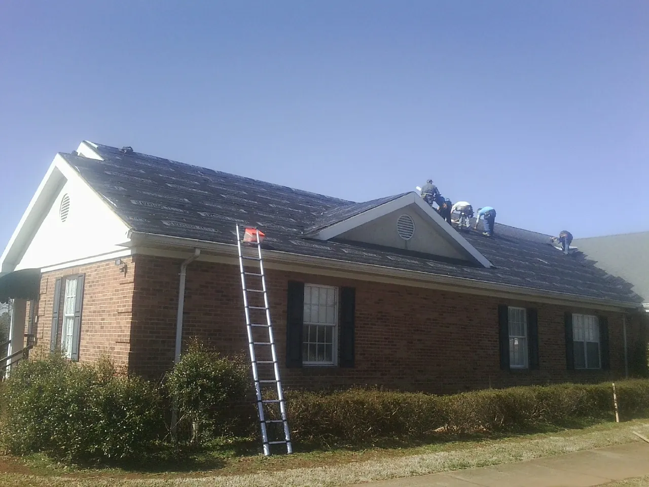 Crew tearing shingles off a brick ranch roof with a ladder set — Metal Roof Repair work by our crew in Limerick
