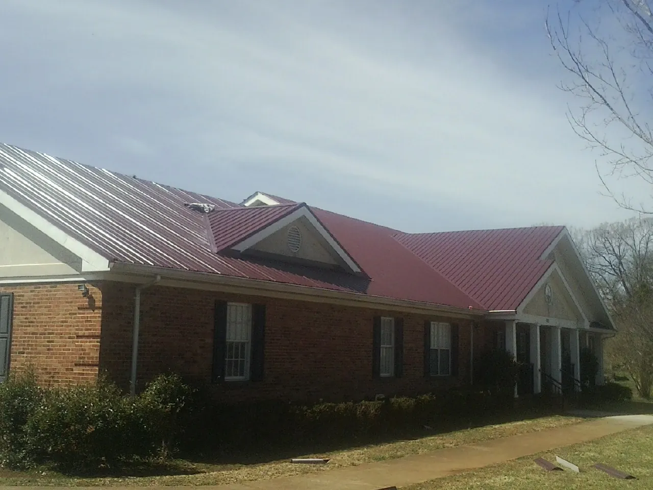 Red metal roof with gabled entries on a long brick building, from a Hail Damage Roof Repair job in Limerick
